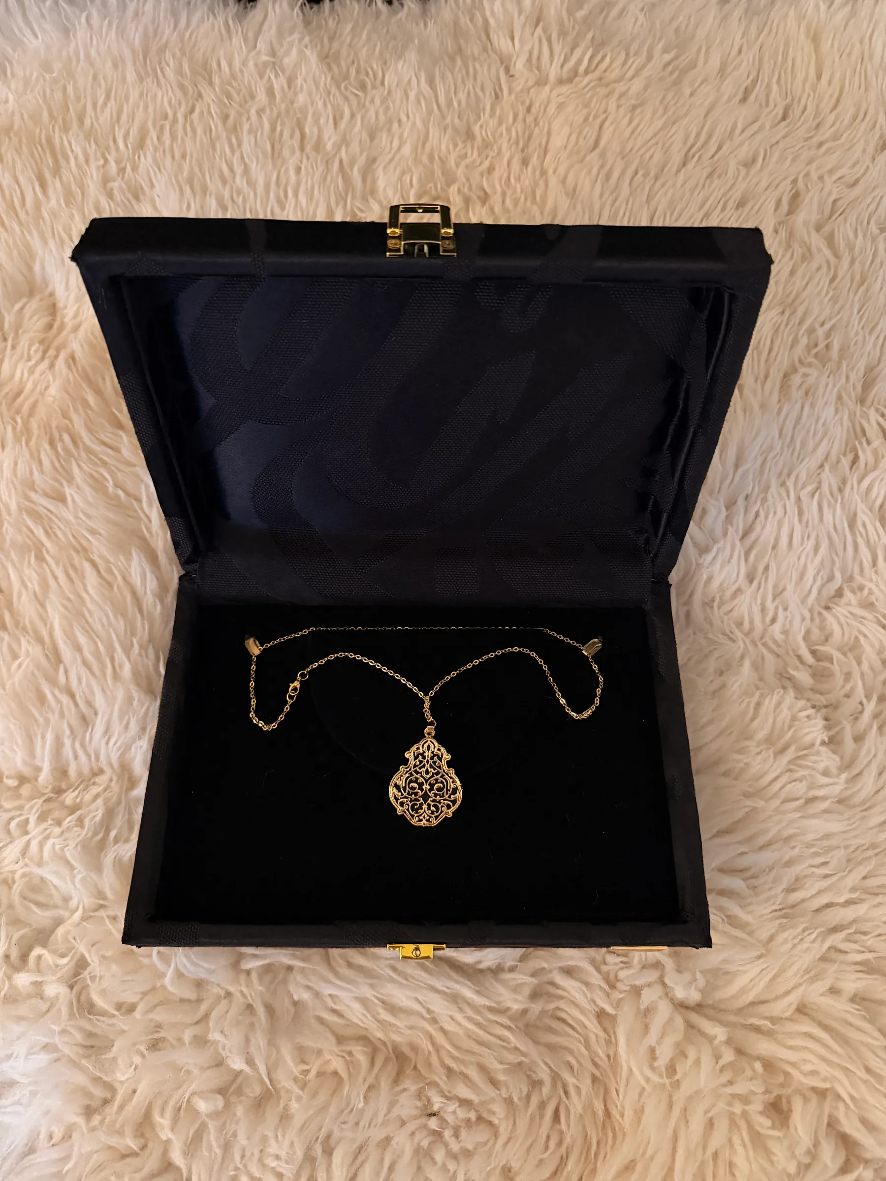 Fine gold-tone necklace with a filigree teardrop pendant in an opened black presentation box