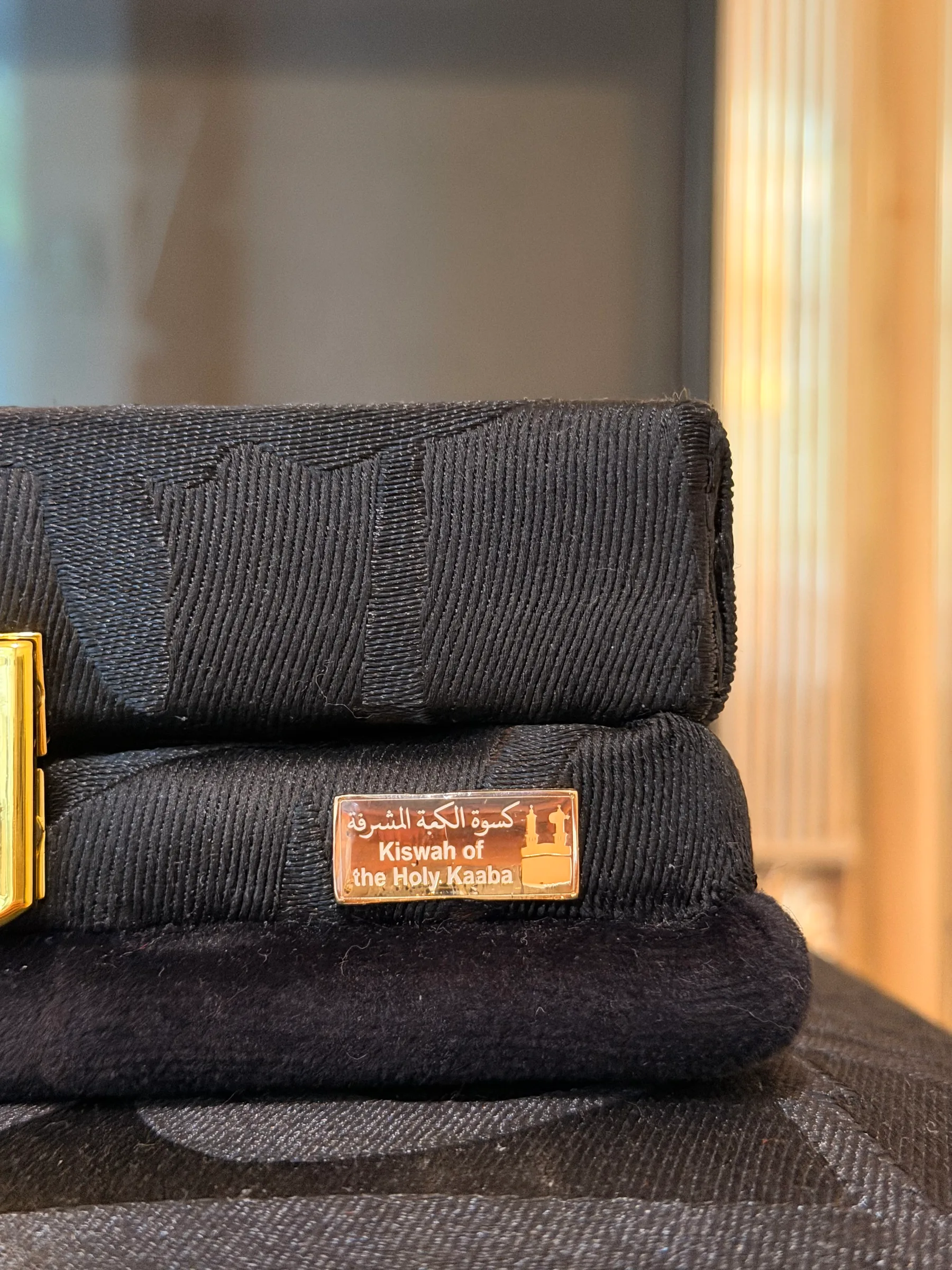 Folded original Kiswah fabric with a gold plaque reading Kiswah of the Holy Kaaba